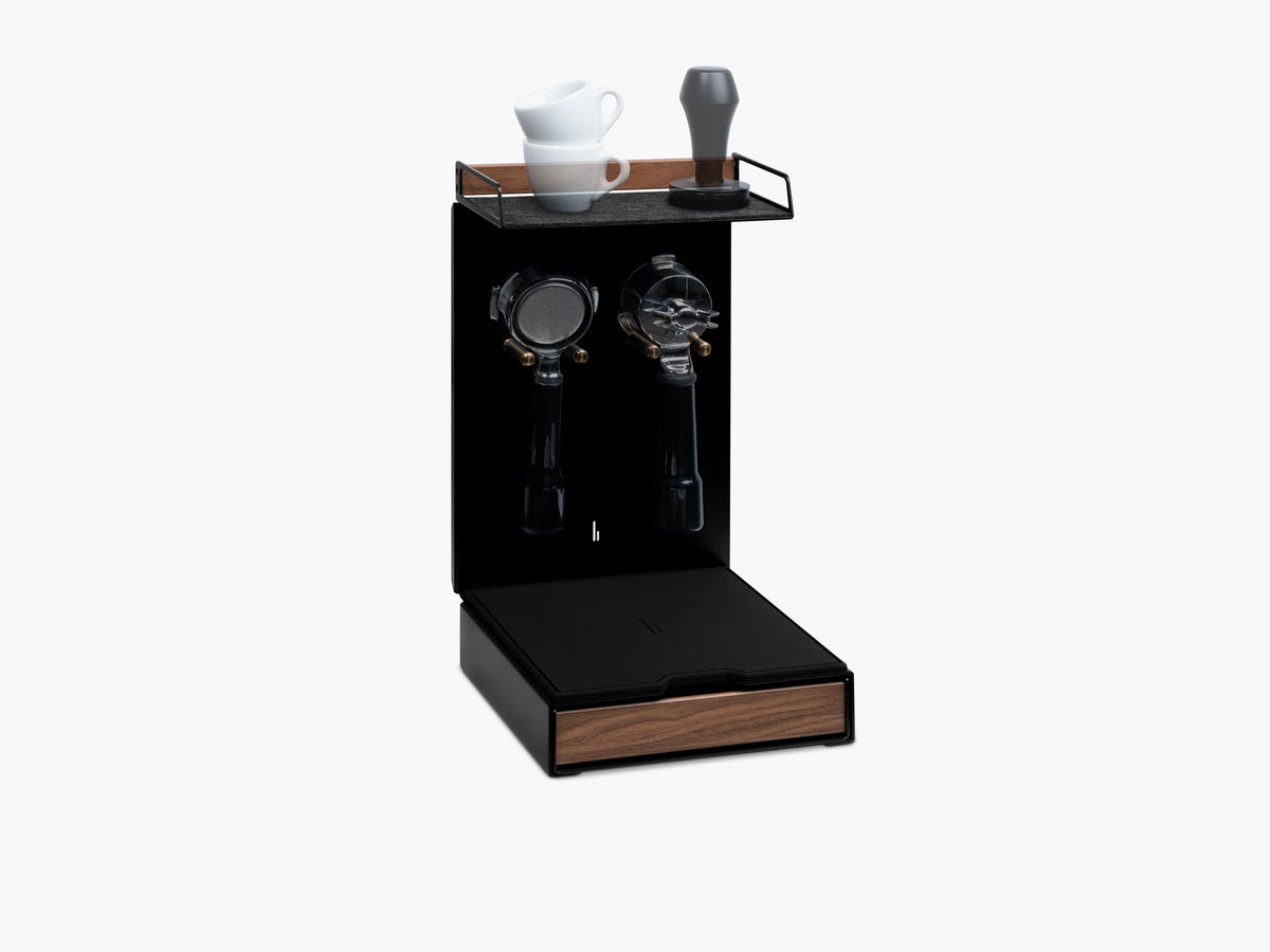 Barista Bar in Schwarz mit Nussbaum-Holzablage, zwei Espressotassen und Tamper auf der Filzauflage, zwei leere Portafilter-Halterungen darunter, Schublade mit Nussbaum-Front @expand #material_Amerikanischer Nussbaum