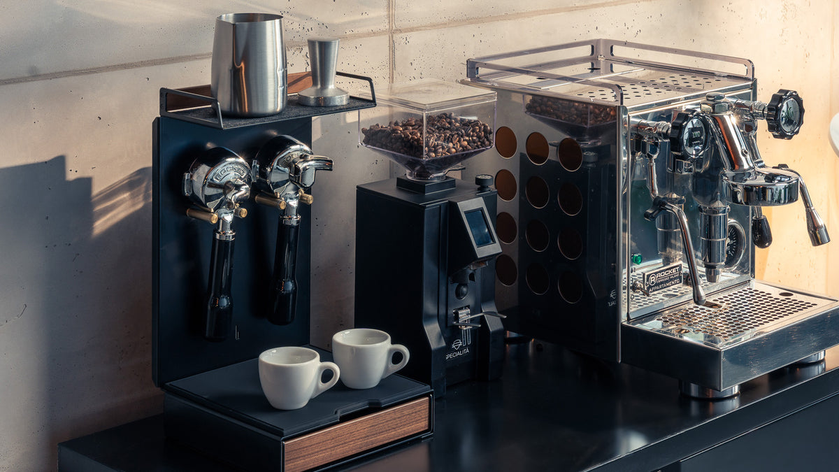 BALOLO Barista Bar in Nussbaum mit zwei Siebträgern, Milchkännchen und Tamper auf der Filzablage, daneben eine Kaffeemühle mit Bohnen und eine Edelstahl-Espressomaschine