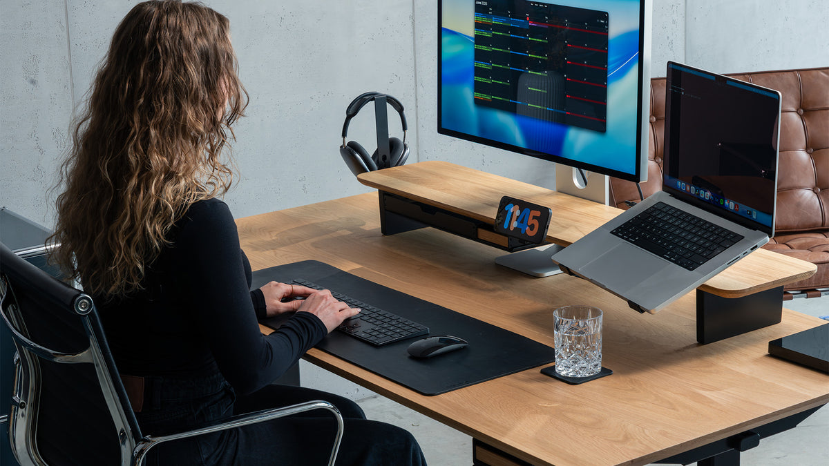 Frau arbeitet am Schreibtisch mit BALOLO Setup Cockpit aus Eiche, Monitor, Laptop und Kopfhörerhalter