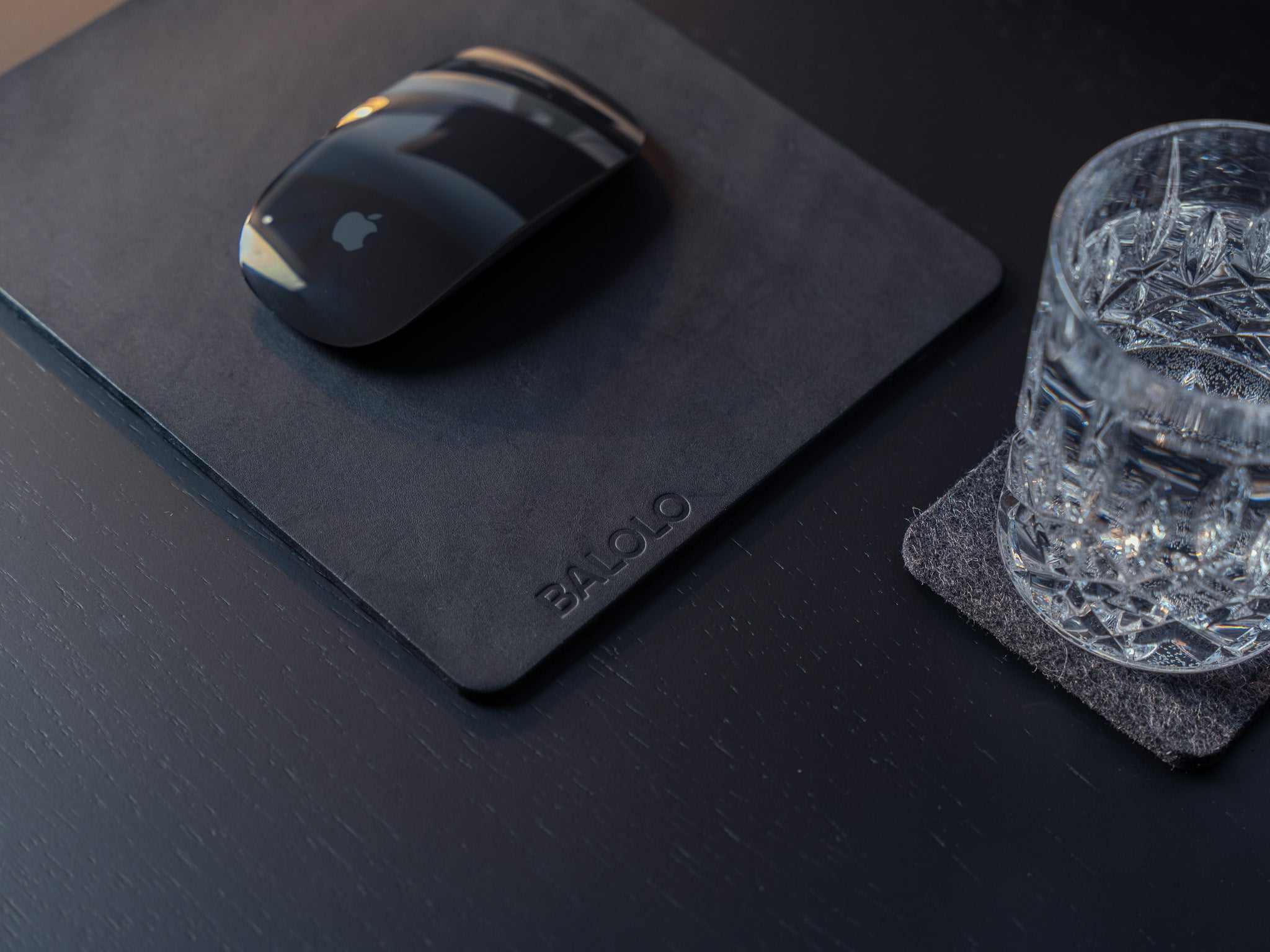 Detailansicht Mauspad Leder auf schwarzem Schreibtisch mit Apple Magic Mouse, Desk Coaster und Wasserglas.