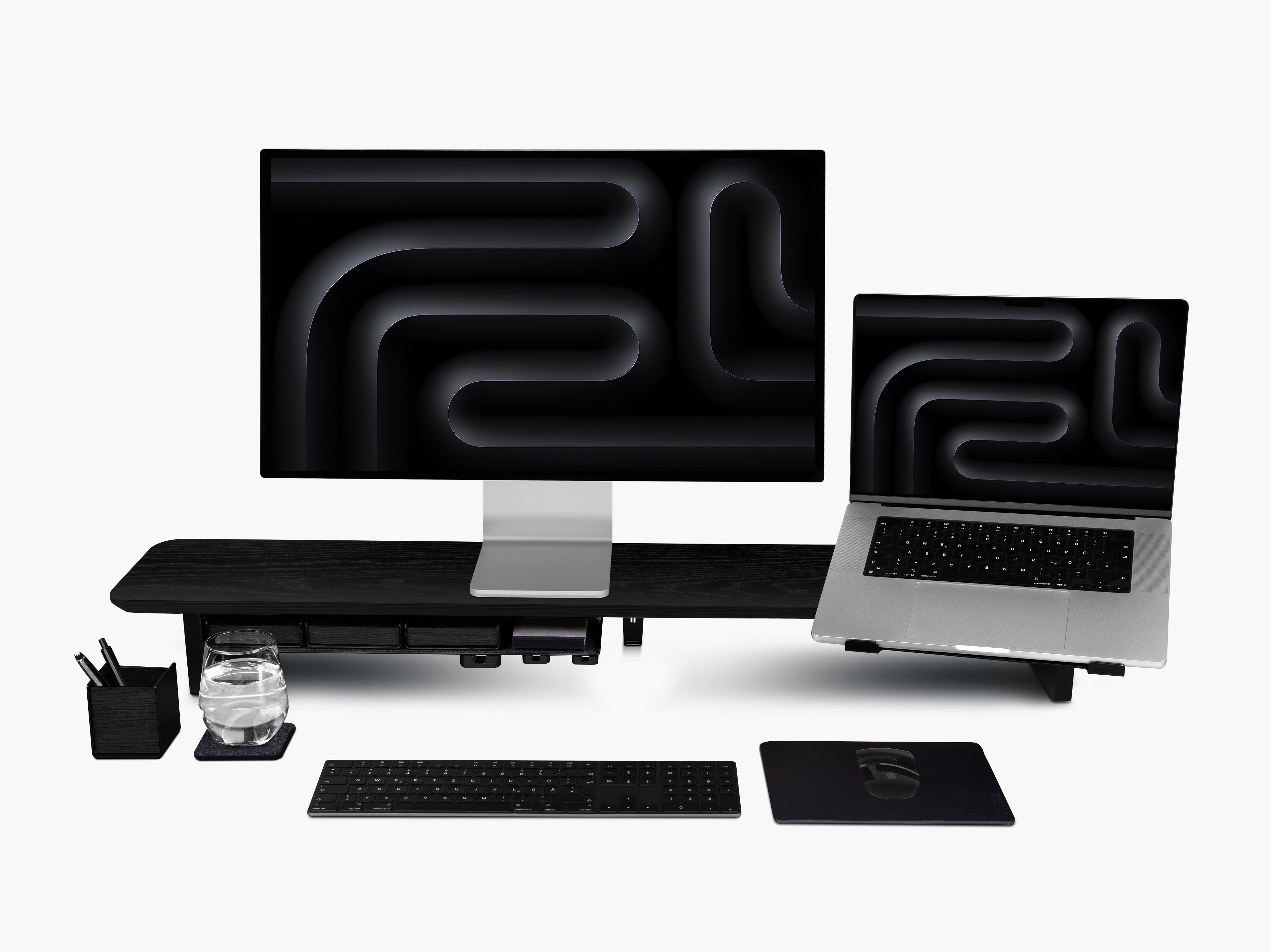 Setup Cockpit Monitorständer aus schwarz gefärbter Eiche mit Anbauteilen: Laptophalter, großes Fach mit Stiftablagen, Kabelmagneten, Mauspad Leder, Desk Coaster, Stifthalter. Abgebildet mit Studio Display, Tastatur und Maus.