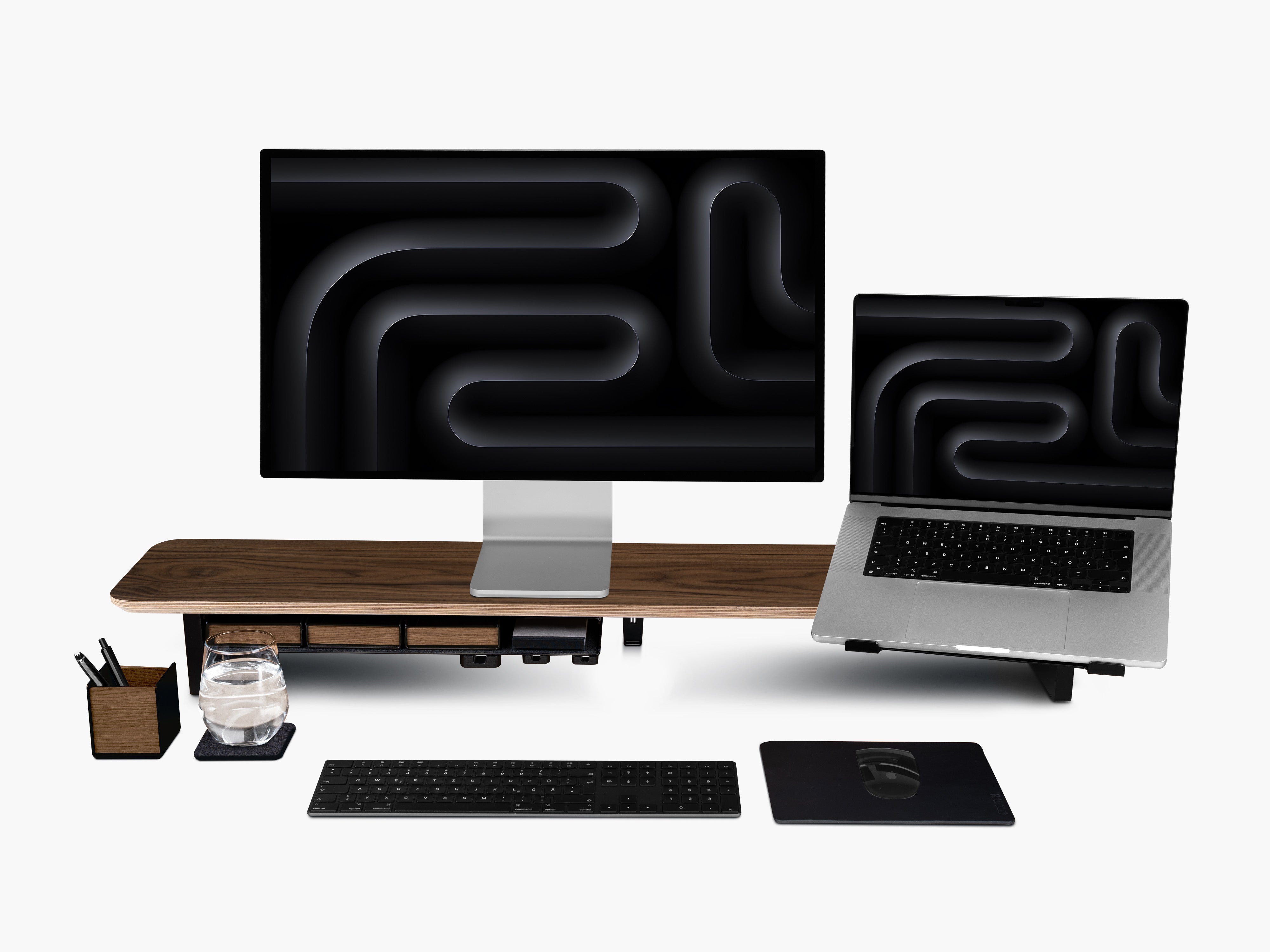 Setup Cockpit Monitorständer aus Nussbaum mit Anbauteilen: Laptop Halter, großes Fach mit Stiftablagen, Kabelmagnete, Mauspad Leder, Stifthalter und Desk Coaster. Abgebildet mit Apple Studio Display, Macbook, Tastatur und Maus.