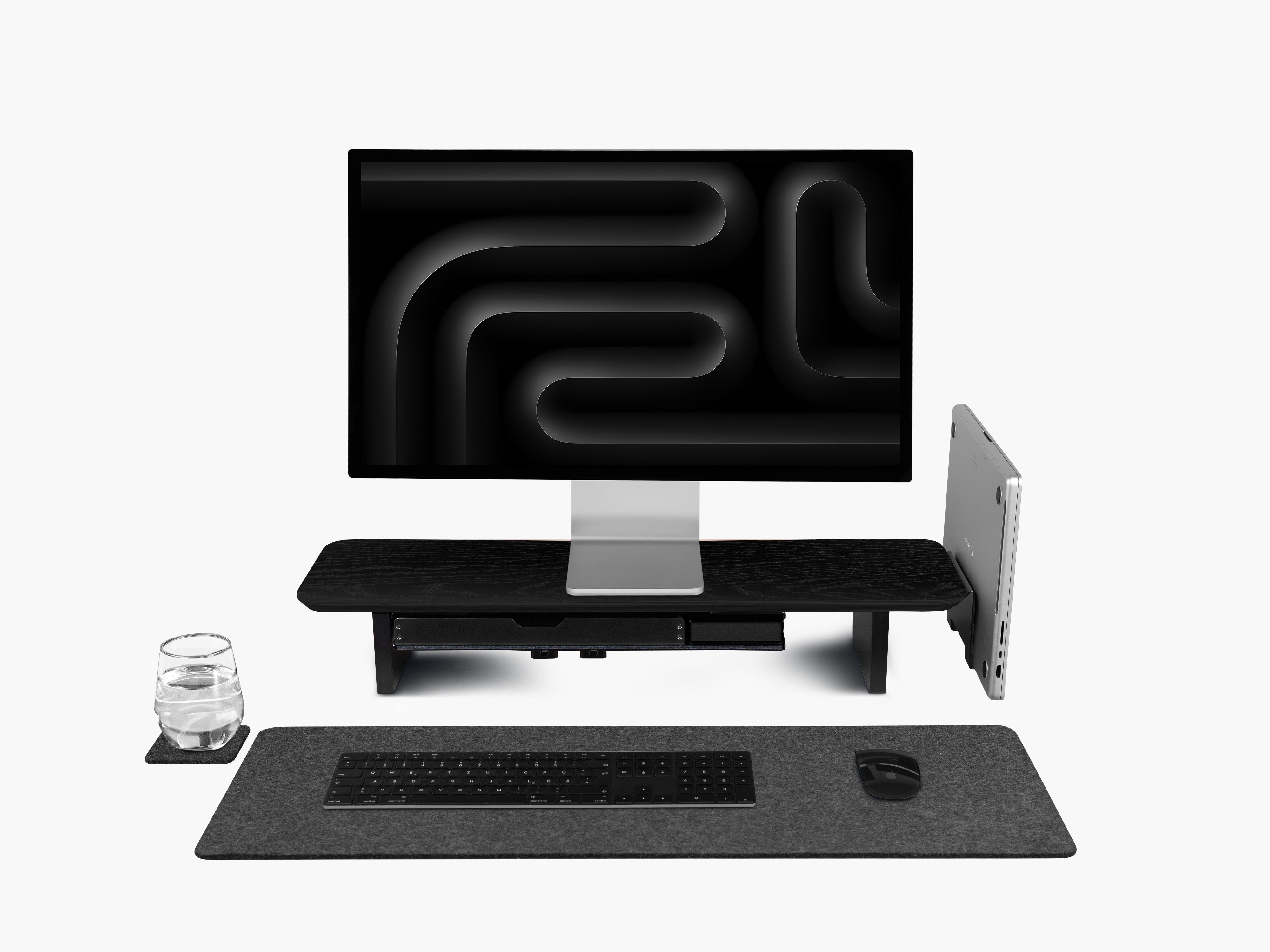 Setup Cockpit Medium aus schwarz gefärbter Eiche mit integrierten Anbauteilen: Laptop Dock, großes Fach, Stiftablage Large und Stiftablage, Kabelmagneten, Desk Pad und Desk Coaster. Abgebildet mit einem Apple Studio Display, Macbook, Tastatur und Maus.