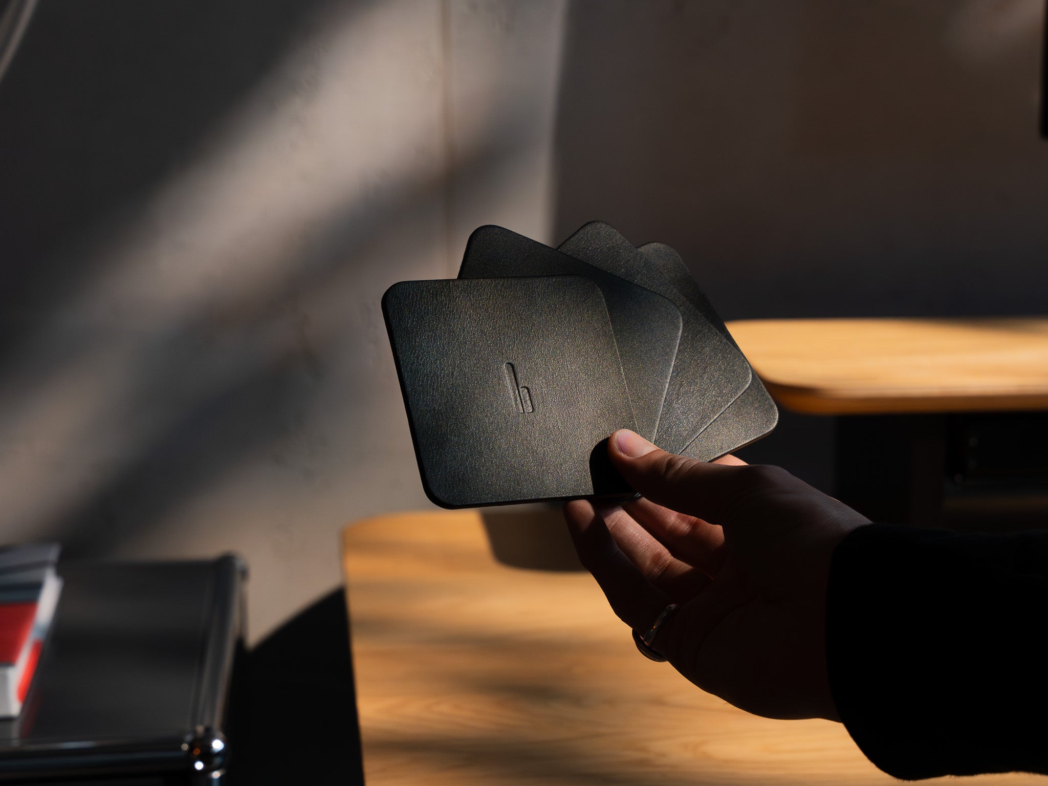 Detailaufnahme der Leder Untersetzer. Person hält vier Untersetzer in der Hand, inszeniert in modernem Office Setting. @expand