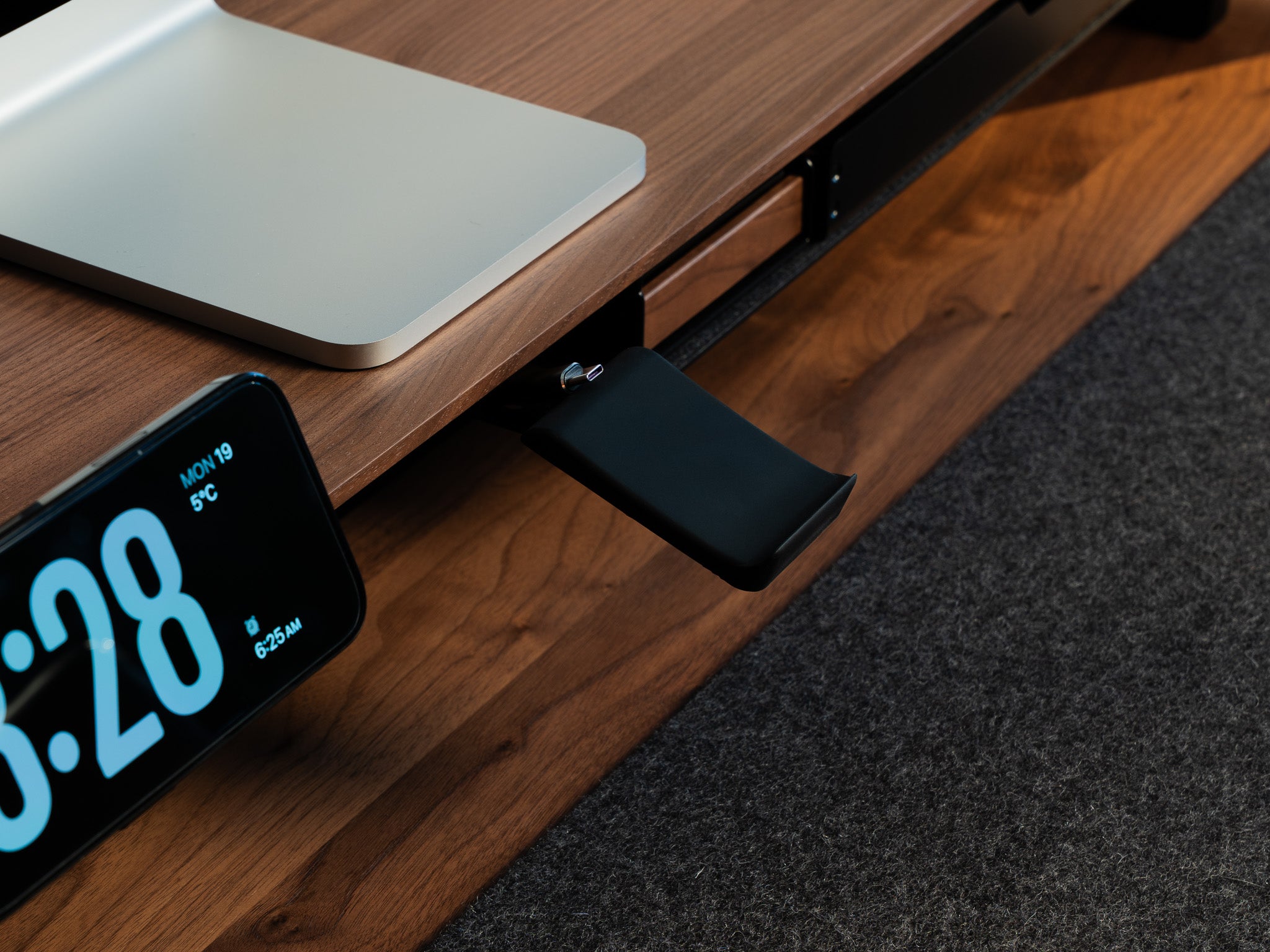 Detail-Aufnahme vom BALOLO Controller Halter montiert am Setup Cockpit Monitorständer in Nussbaum. In ästhetischem Office-Setup, Hand nimmt in Bewegung einen PlayStation 5 Controller aus der Controller Halterung.