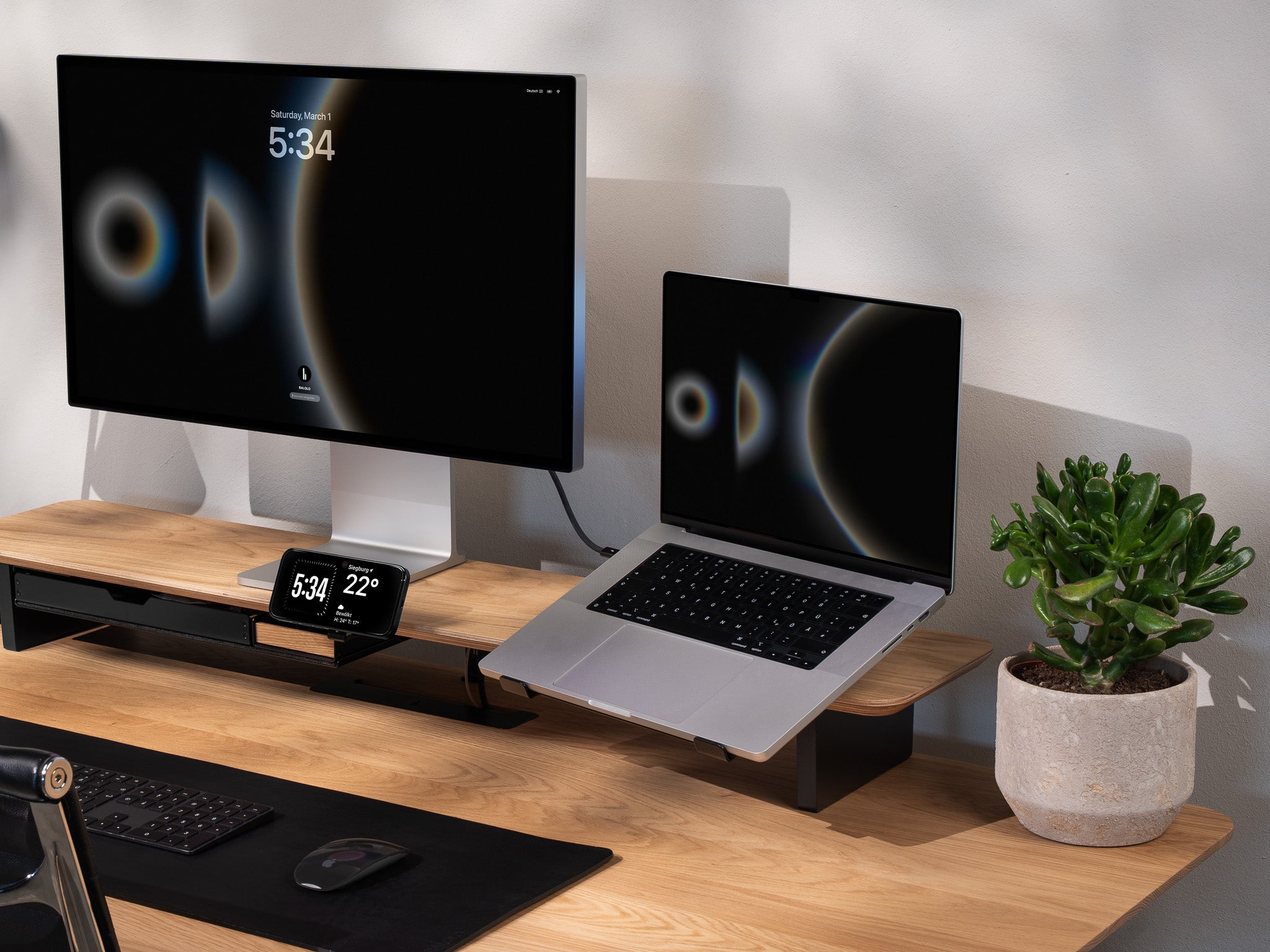 BALOLO Laptophalter montiert am Setup Cockpit Monitorständer mit einem Macbook in der Halterung. Setup ergänzt durch Apple Studio Display und iPhone in modernem Office Setting.